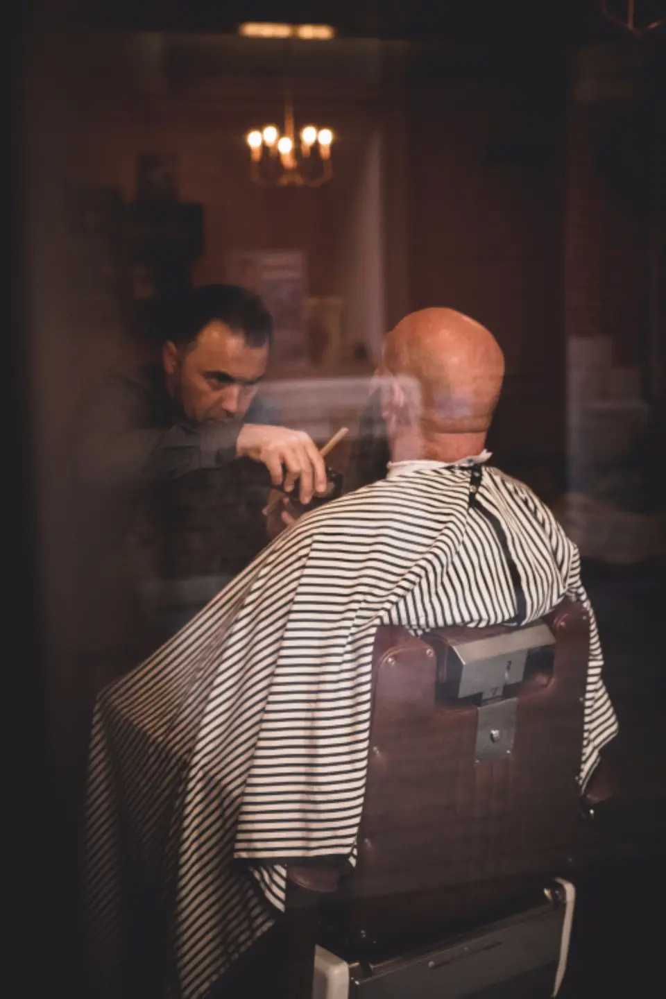 Barber trimming a customer’s hair beside a sunny shop window